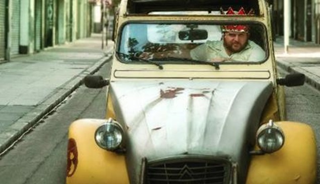 Scene from The Tenth Man, with Ariel driving an old yellow car while wearing a Purim crown